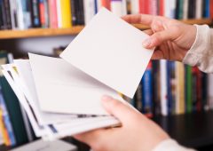Femal hands holding postcards. In the back a bookshelf with a lot of books.More like this: